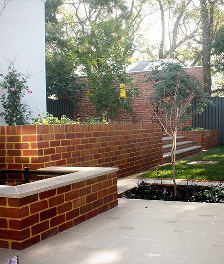 Feature brick retaining wall, seating ledge and paving beside a garden bed