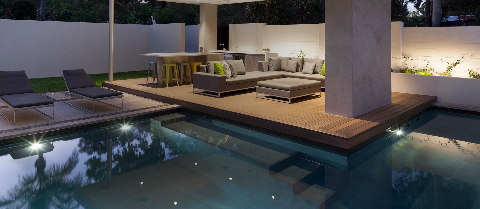 Poolside alfresco deck and outdoor living area at dusk, a Transforming Homes and Gardens landscape build