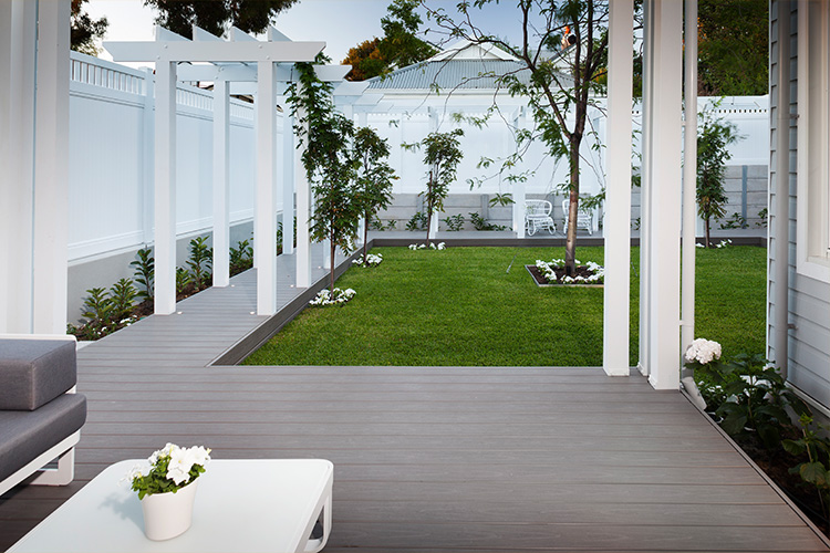 White pergola walkway over a timber deck bordering a manicured lawn